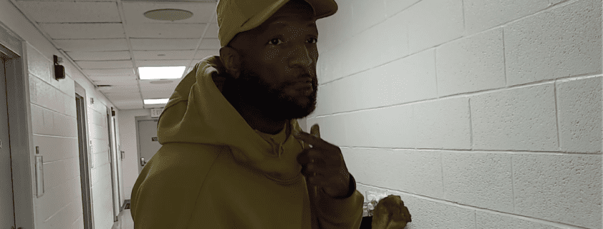 Man in hallway wearing a hoodie, hat.